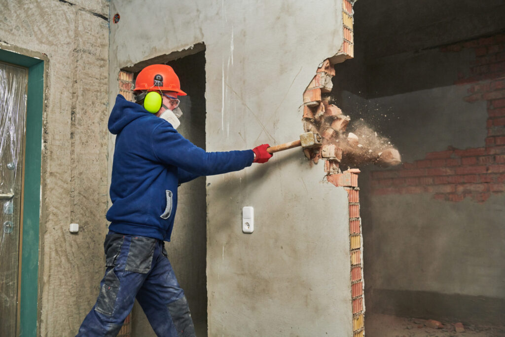 A construction worker demolishes a wall with a mallet